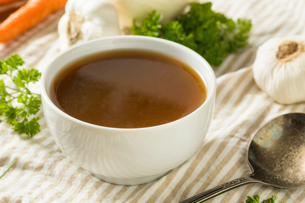 Beef broth in a white bowl around aromatic herbs.  It is important to use your senses when determining if beef broth has gone bad.