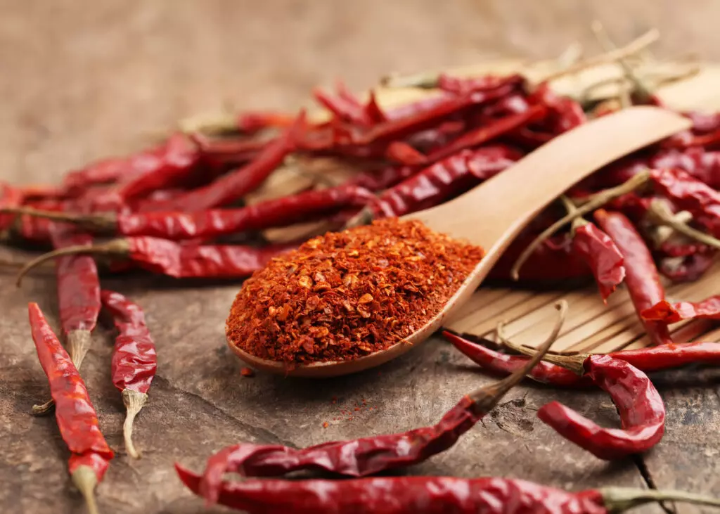 Ground cayenne pepper on a wooden spoon with whole dried  cayenne peppers 