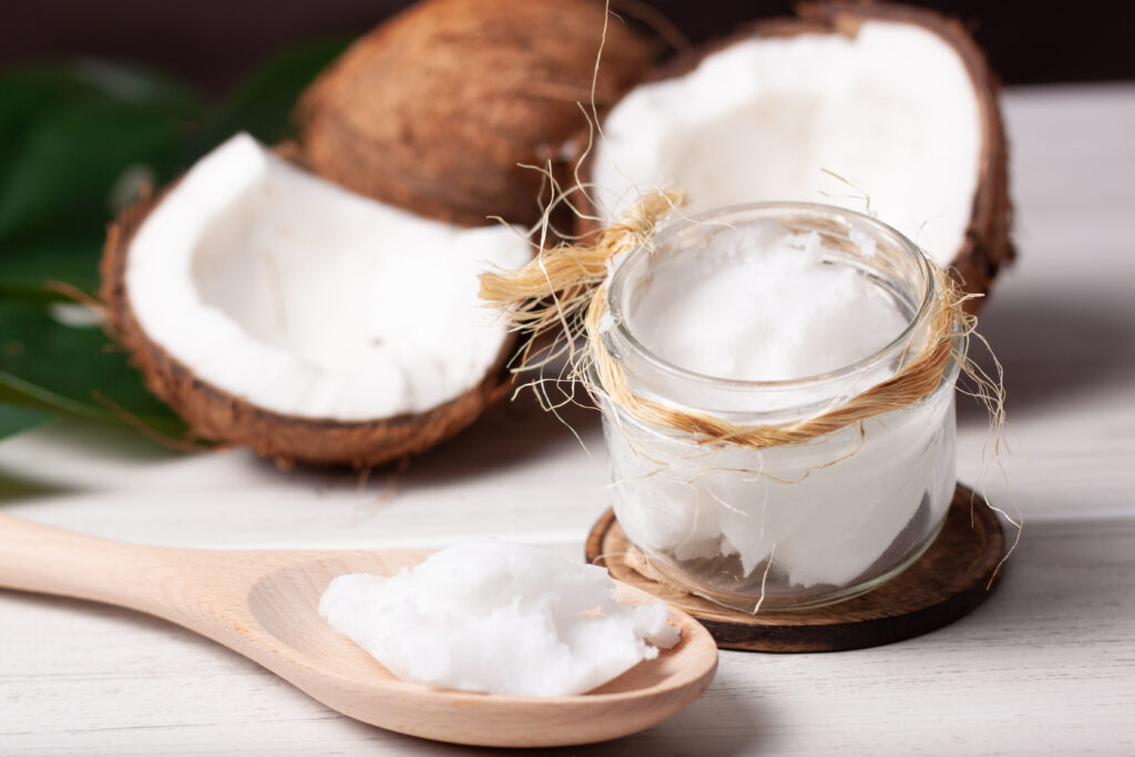 Coconut oil in a jar next to coconuts and a wooden spoon. 