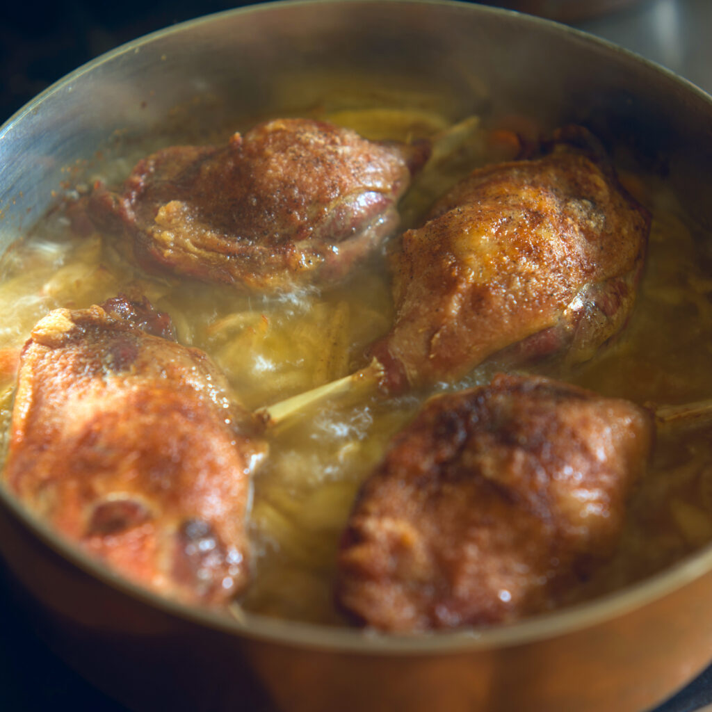 Close up of duck thighs cooking in duck fat.  The rich meaty flavor of duck fat make it a great substitute for bacon grease. 