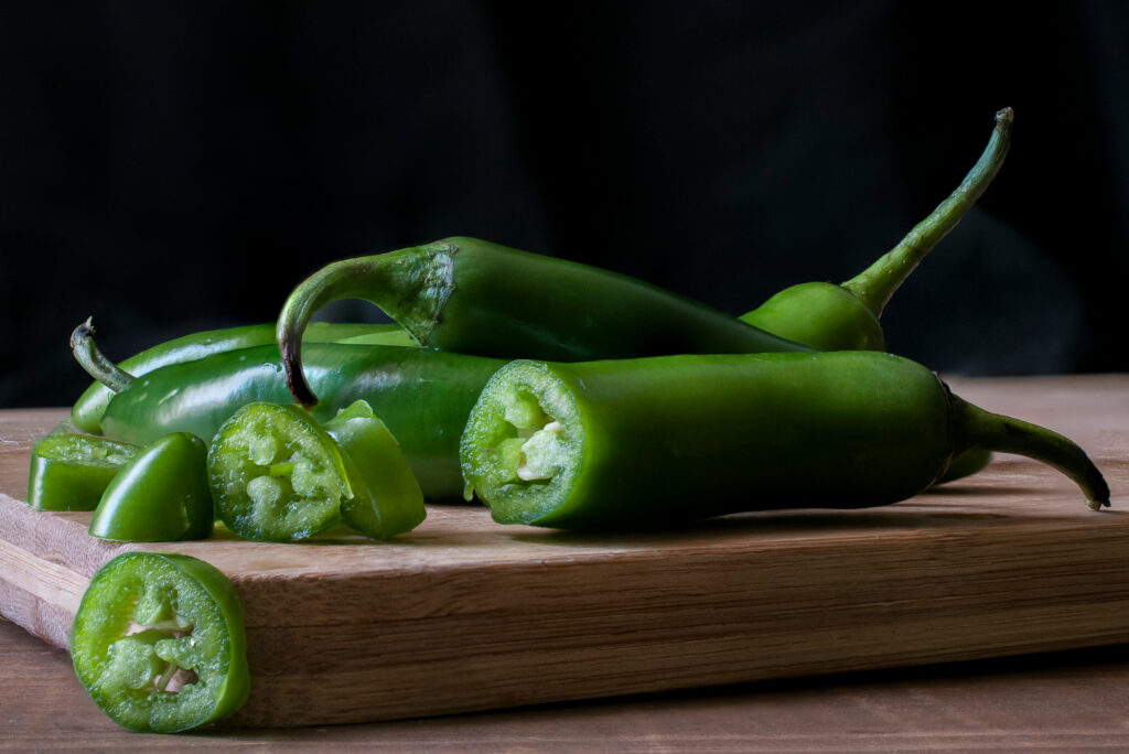 Sliced and whole Serrano peppers on a cutting board.  Their texture and color make them a popular jalapeño pepper substitute.