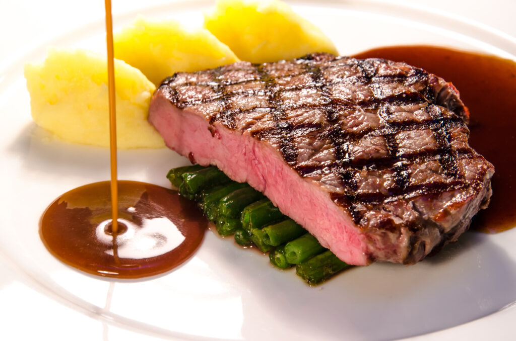 Close up of steak sauce next to a medium steak on a plate