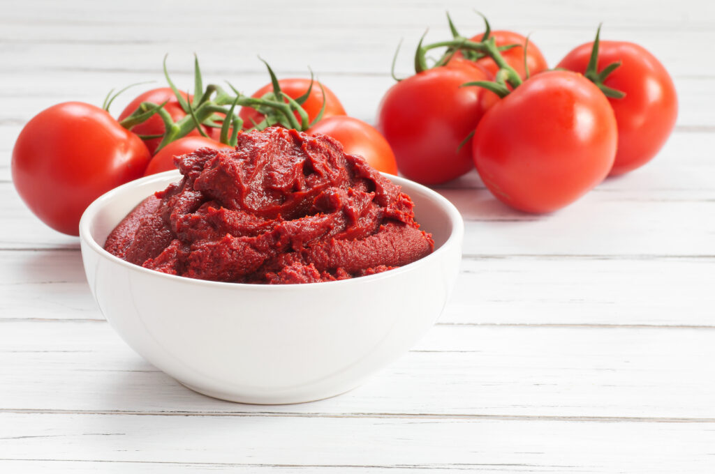 Tomato paste in a bowl alongside tomatoes connected to vines.  Deep and rich flavors make this a great substitute for beef broth.