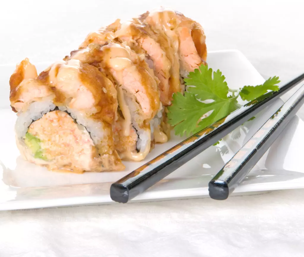 Close up of an Alaska roll using cooked salmon and a crab salad filling drizzled with a sriracha mayo sauce.