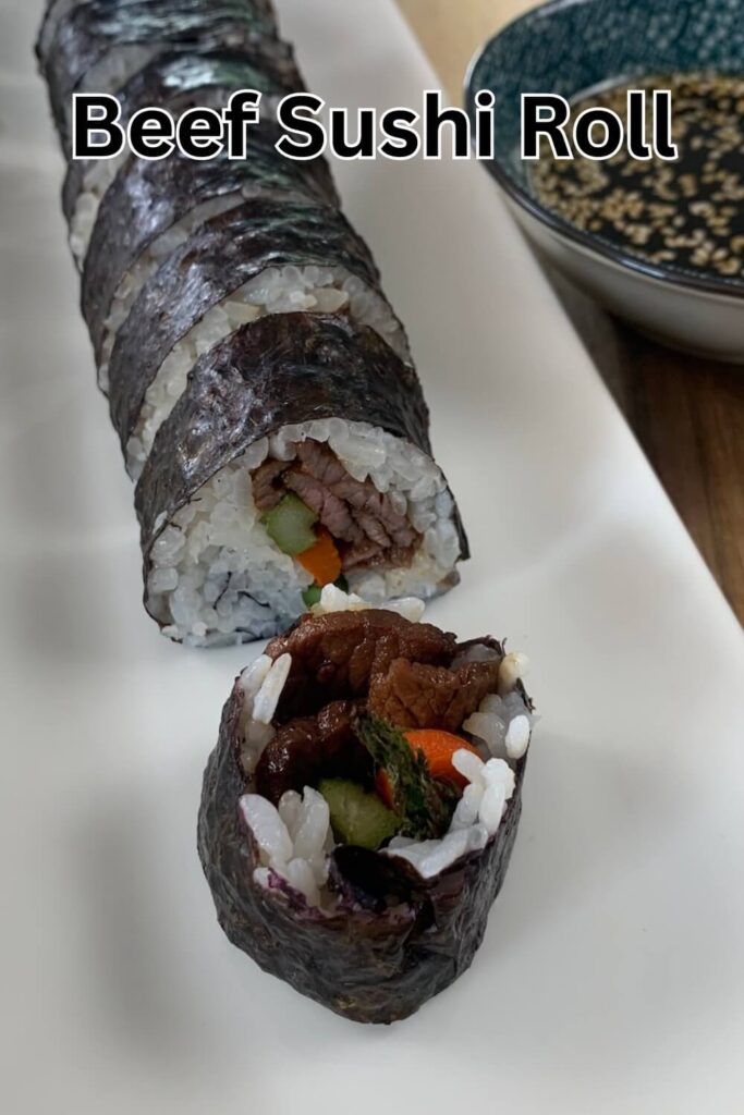 Beef sushi roll vertical pic on a white sushi platter with a ramekin of yakiniku sauce in the background.