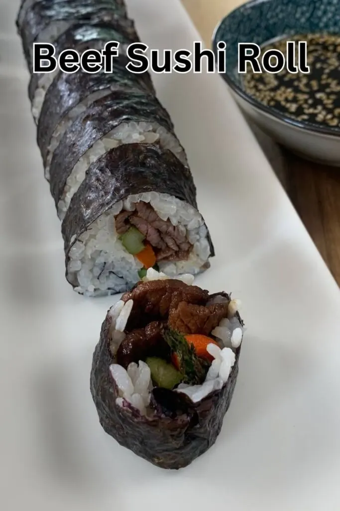 Beef sushi roll vertical pic on a white sushi platter with a ramekin of yakiniku sauce in the background.