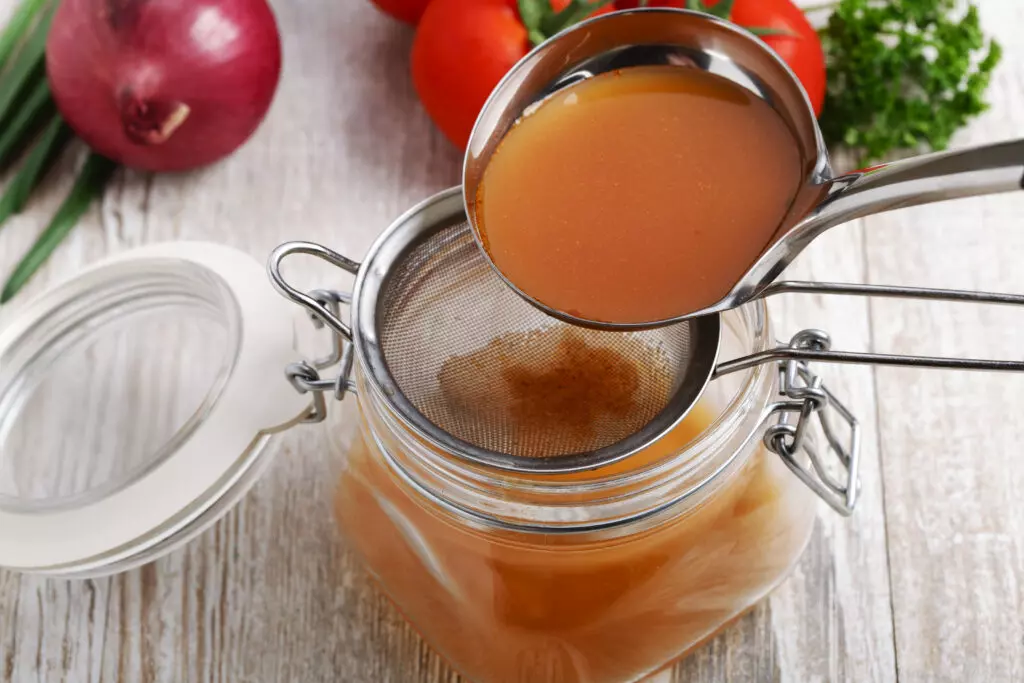 Beef broth in a jar surrounded by tomatoes, onions and aromatic seasonings. 