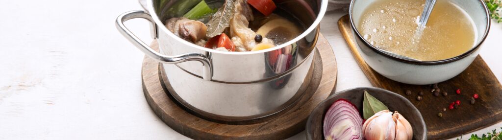 Beef broth simmering in a pot with vegetables, aromatics and beef bones