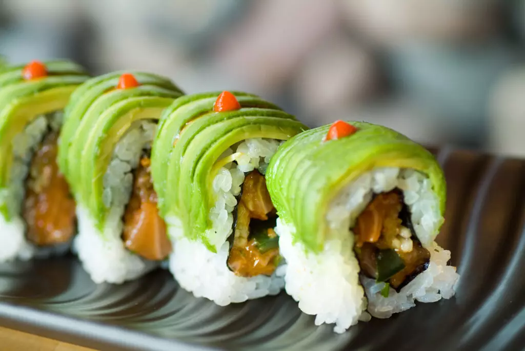 Caterpiller rolls arranged on a black plate.  Like the Dragon Roll, Caterpillar rolls are a fun cooked sushi to enjoy with your kids.