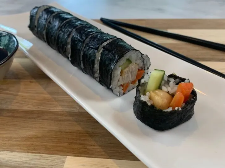 Chicken teriyaki roll on a white sushi plate with teriyaki sauce and chopsticks in the background.