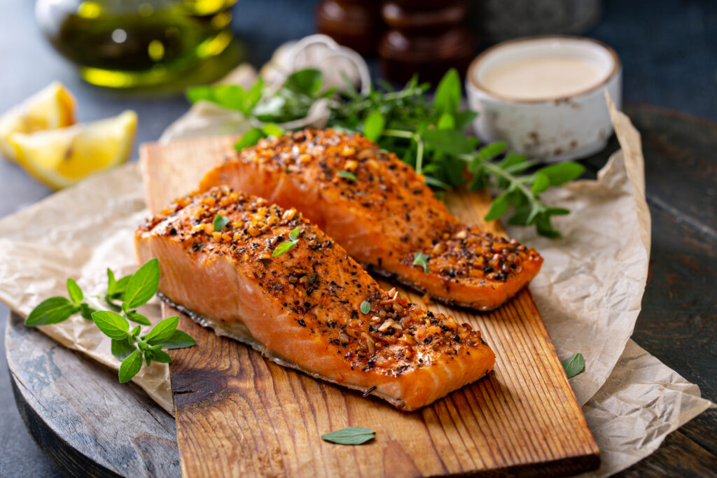 Cooked salmon on a cutting board with herbs and lemon in the background.  Salmon can be stored in the freezer.