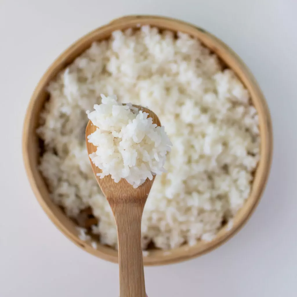 Close up view of sushi rice in a bowl with a wooden spoon.