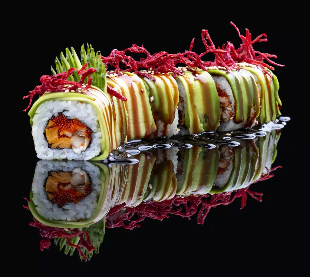 Colorful Dragon roll sushi with a black background.  Dragon rolls are a fun cooked sushi roll to enjoy with your kids.