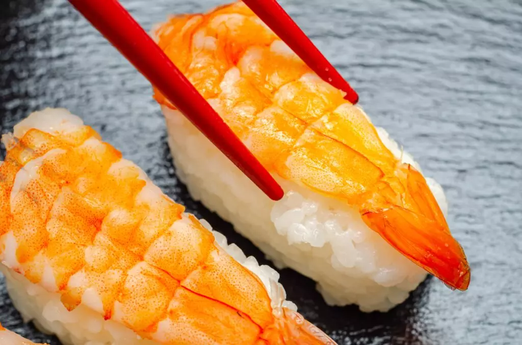 Close up of ebi sushi being picked up by a chopstick.