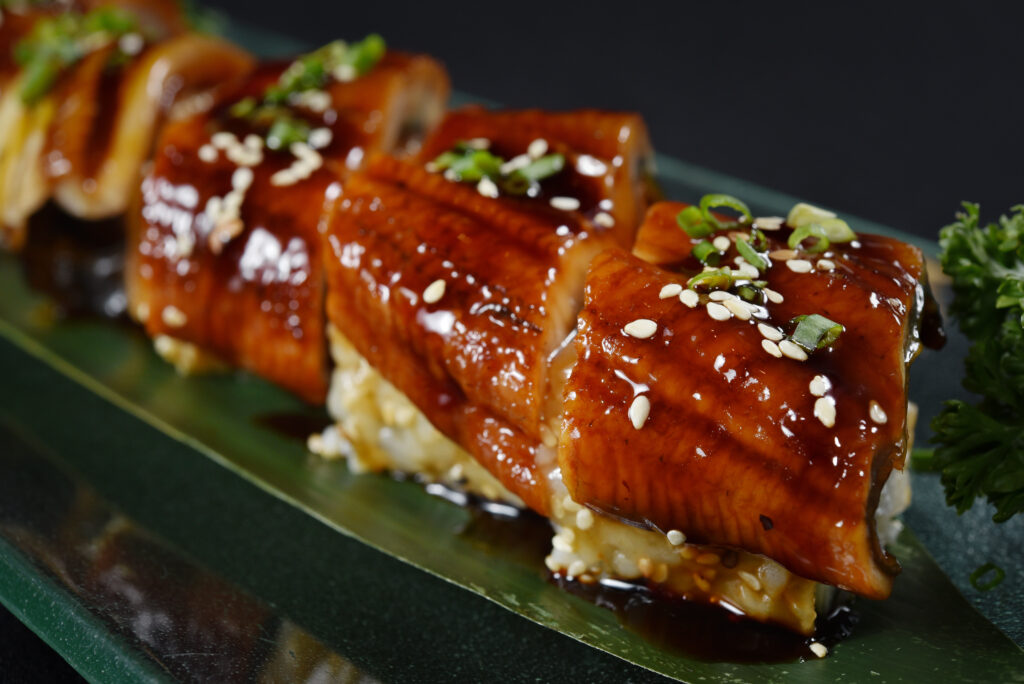 Unagi (or eel) roll arranged on a sushi platter topped with unagi sauce, sesame seeds and green onions.