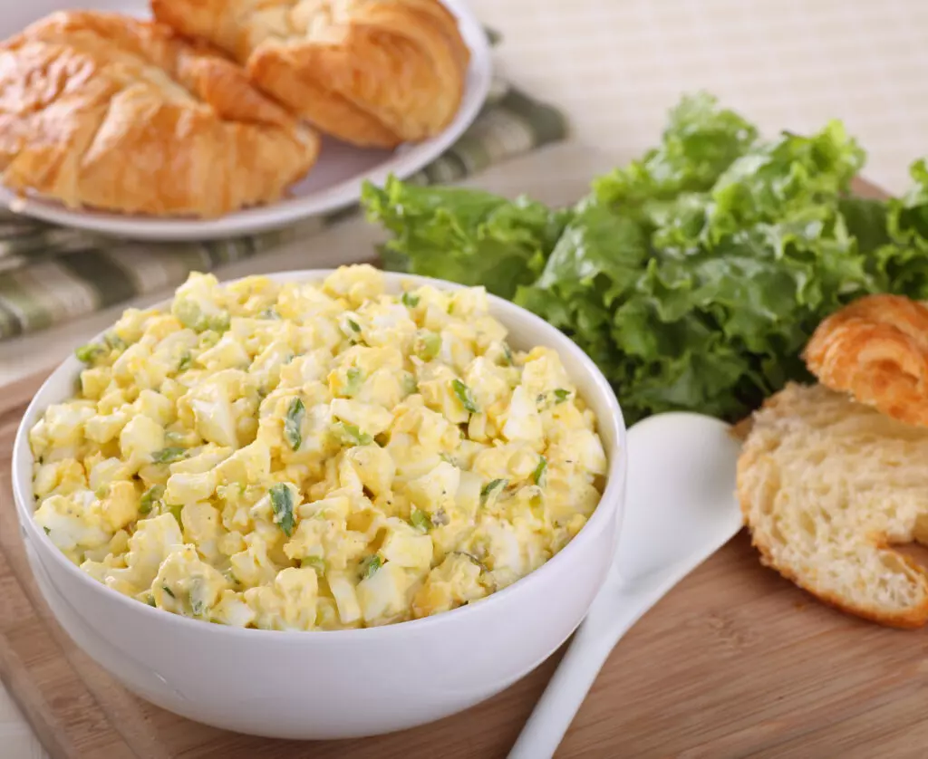 Egg salad in a bowl with croissants and lettuce