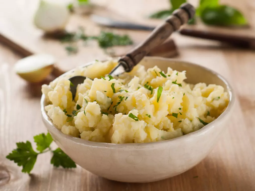 Close up of butter mashed potatoes with herbs in a bowl. 
