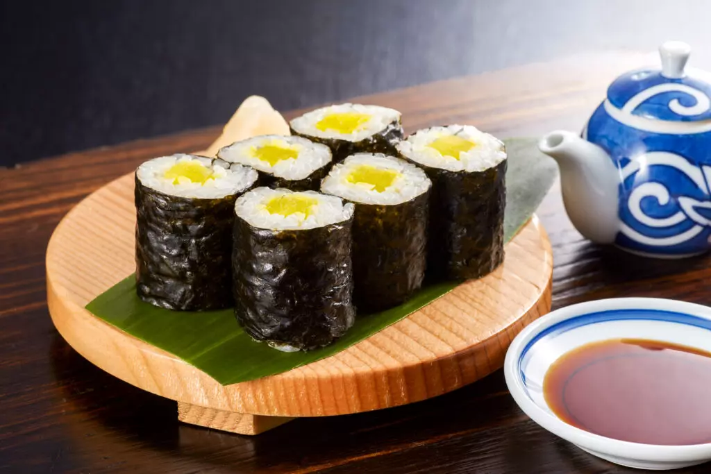 Oshinko rolls on a platter with a tea pot and a bowl of soy sauce