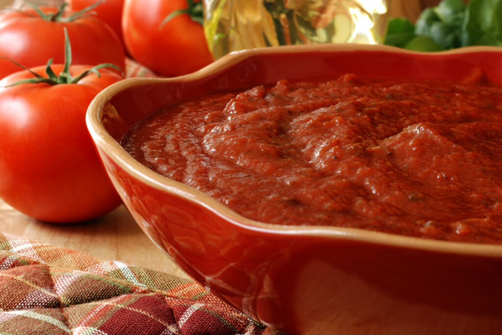 Pasta sauce in a large bowl with tomatoes in the background