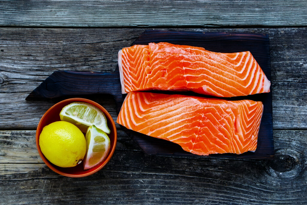 Slabs of raw salmon on a cutting board with a bowl of lemons and limes. 