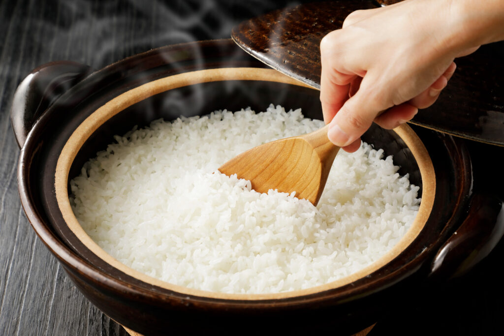 Hot sushi rice in a bowl being stirred by a wooden spoon.
