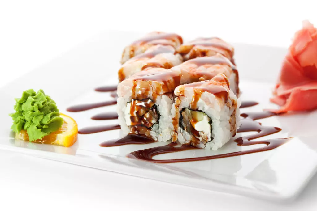 Unagi sauce (eel sauce) drizzled over uramaki sushi rolls.  Served on a white plate with pickled ginger and wasabi