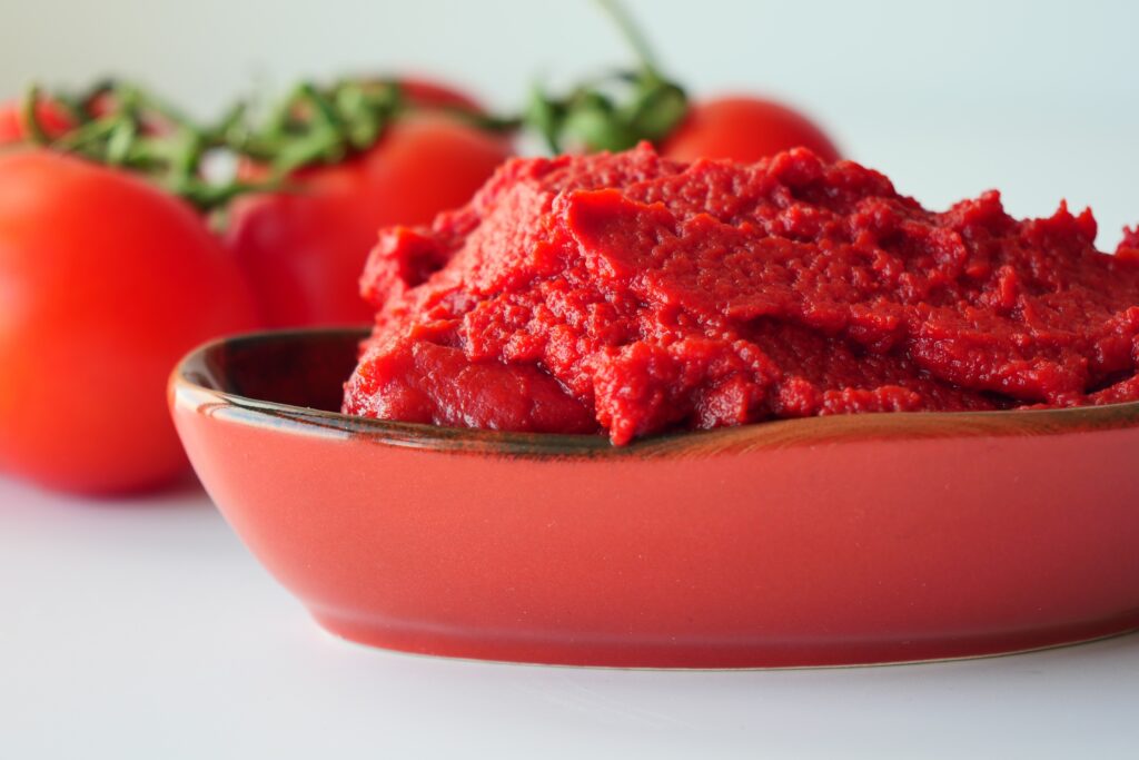 Close up of tomato paste in a bowl with fresh tomatoes in the background
