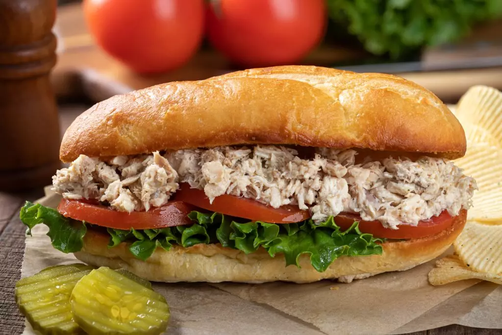 Tuna salad on a sub sandwich with chips and pickles.  Knowing the best methods for saving tuna salad is important for preventing food bourn illness. 