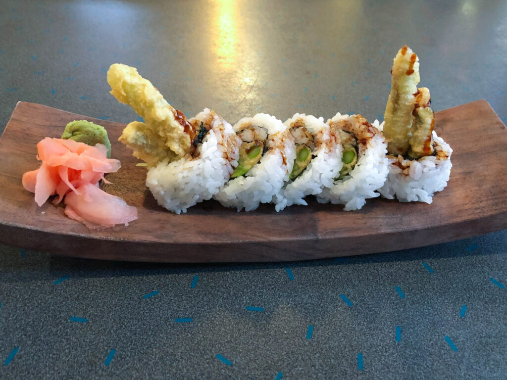 Vegetable tempura rolls arranged on a wood platter served with wasabi and pickled ginger.  This is also a great sushi option for vegetarians.