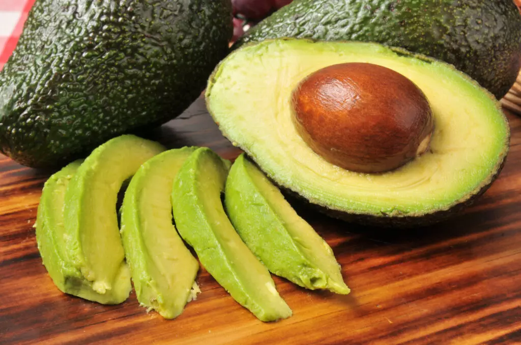 Close up of sliced avocado with some whole avocados in the background.