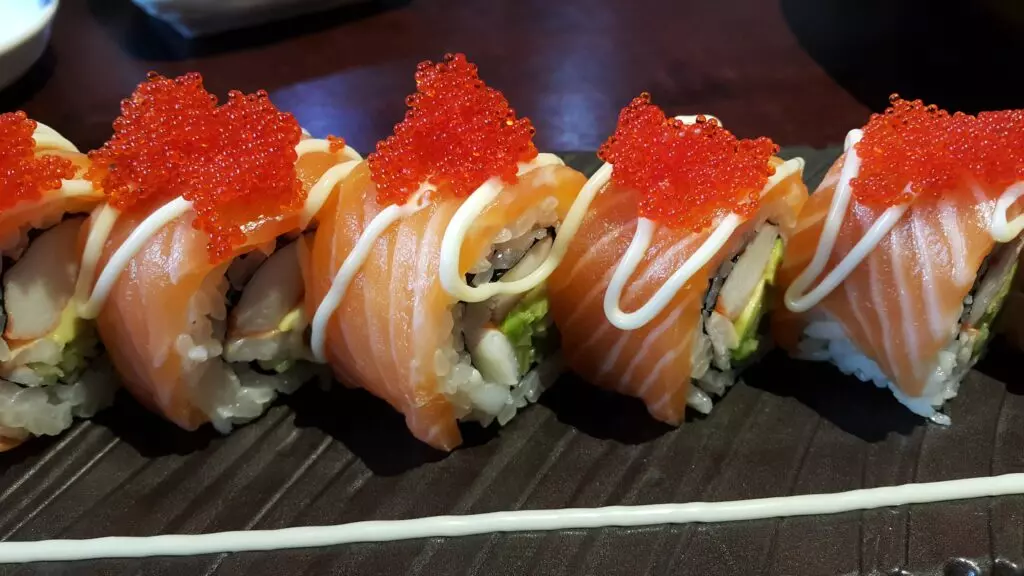 Alaska rolls arranged on a plate with Japanese mayo drizzled over the top and a tobiko garnish.