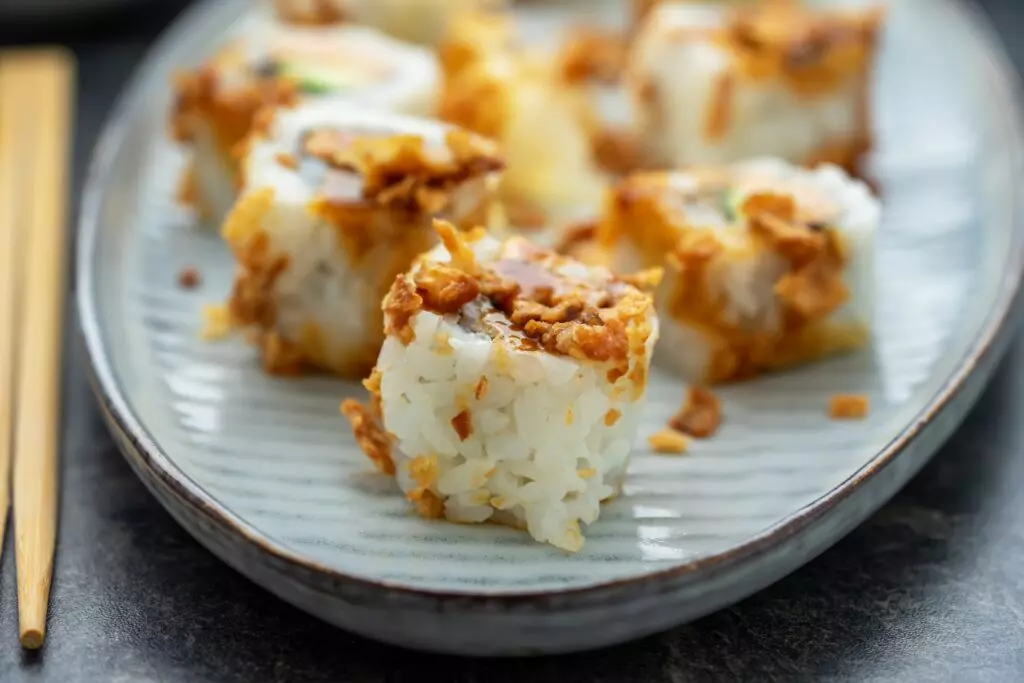 Close up view of crunchy California rolls on a plate with chopsticks.
