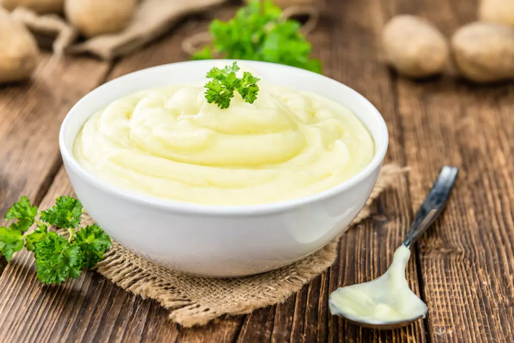 Mashed potatoes in a bowl garnished with parsley and with whole potatoes in the background.  Freezing mashed potatoes is a great way to preserve them.