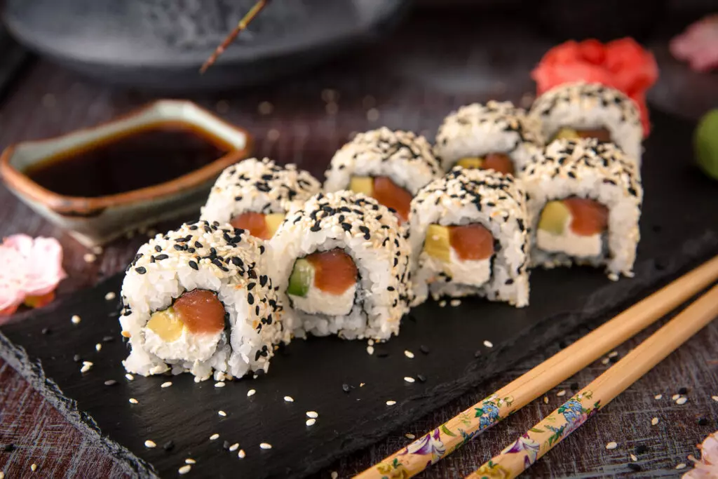 Philadelphia rolls on a black platter with ginger, wasabi, soy sauce and chop sticks