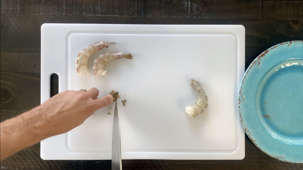 Using knife to scrape black liquid out of the tail of the shrimp