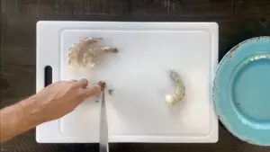 Using knife to scrape black liquid out of the tail of the shrimp
