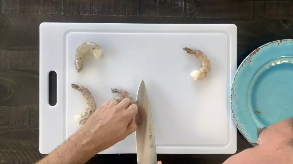 Cut slice in back of shrimp exposing vein.  Scrape vein out of shrimp.