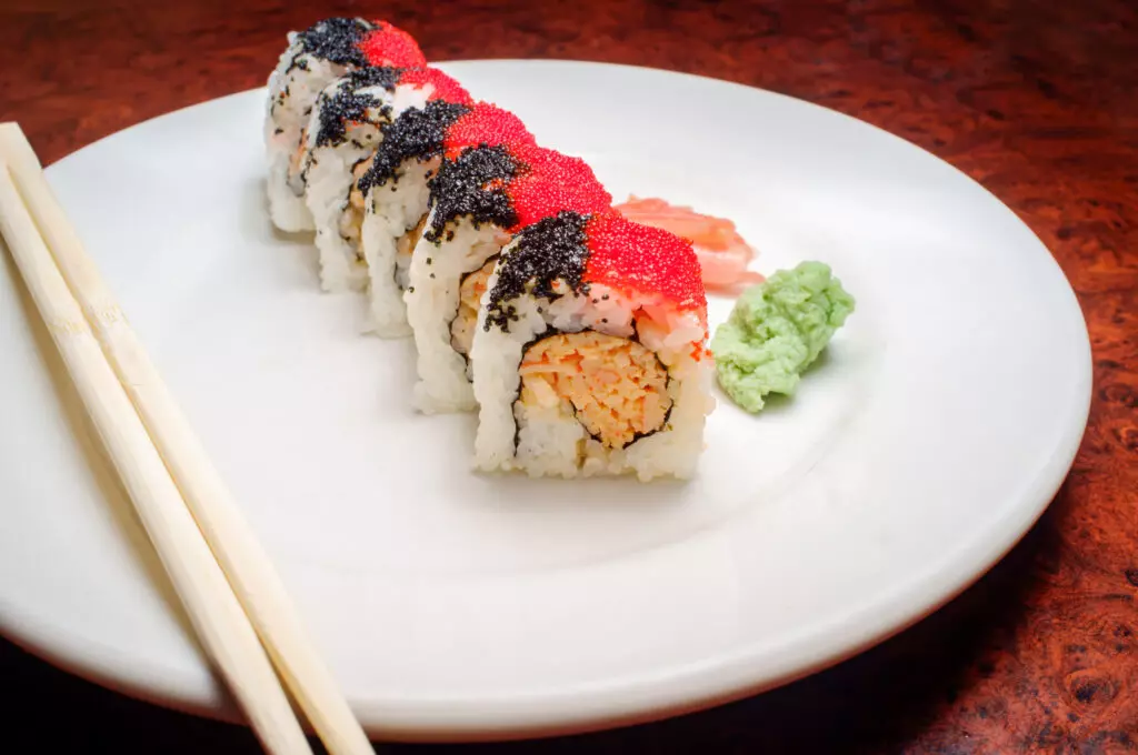 Spicy crab roll garnished with tobiko and sesame seeds on a white plate with chopsticks, wasabi and ginger