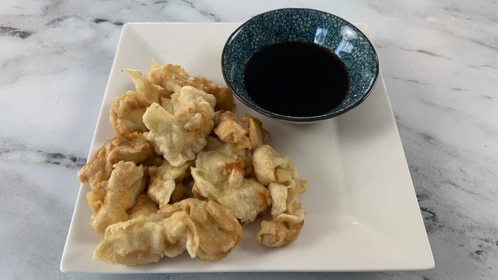 Chicken tempura on a white plate with tempura dipping sauce. 