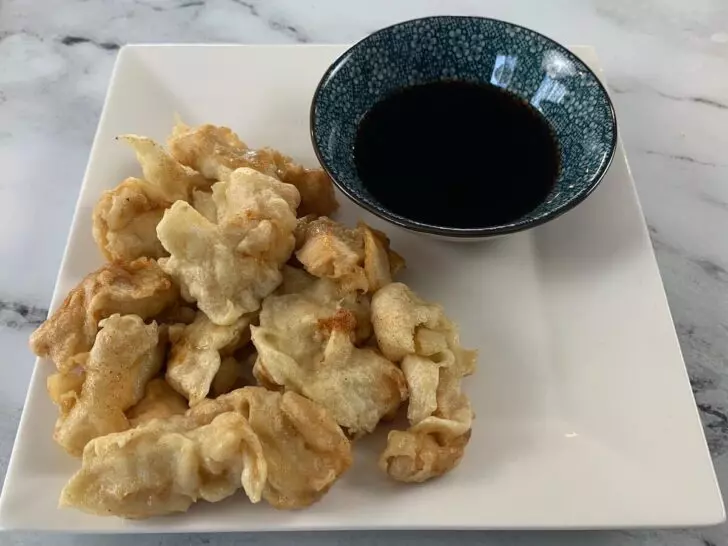 Finished chicken tempura on a white plate with tempura dipping sauce.