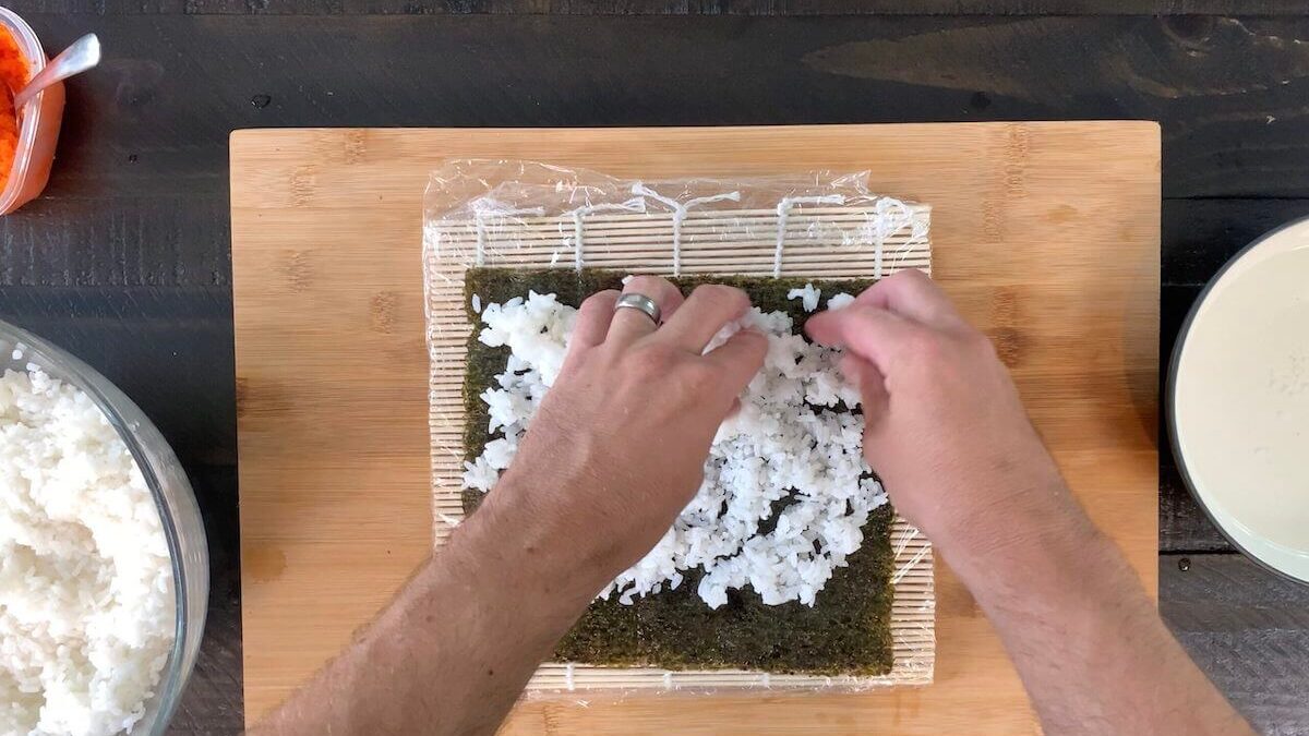 Pressing the sushi rice onto the nori sheet.