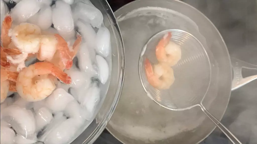 Removing shrimp from water and adding to ice to quickly stop shrimp from cooking.