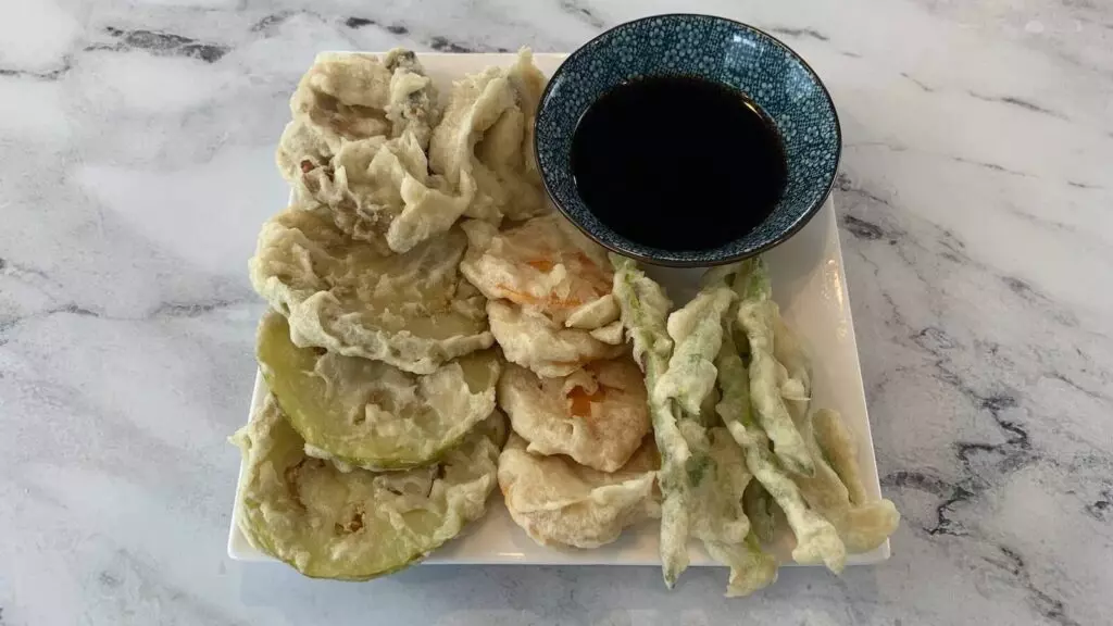Vegetable tempura arranged on a white plate with a bowl of tempura dipping sauce (tentsuyu).