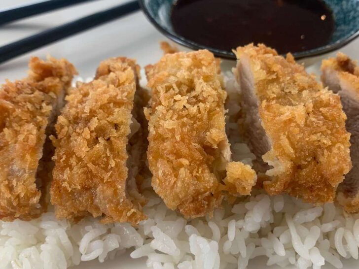 Chicken katsu on a bed of rice with katsu sauce and black chopsticks in the background.