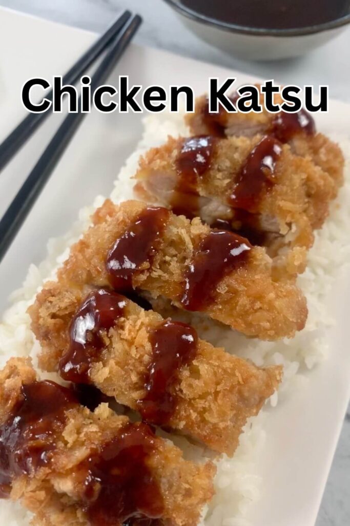 Close up vertical shot of chicken katsu on a bed of rice drizzled with katsu sauce with chop sticks and a ramekin of katsu sauce in the background. 