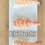 Close up shot of ebi sushi (shrimp sushi) on a white plate with a bamboo cutting board