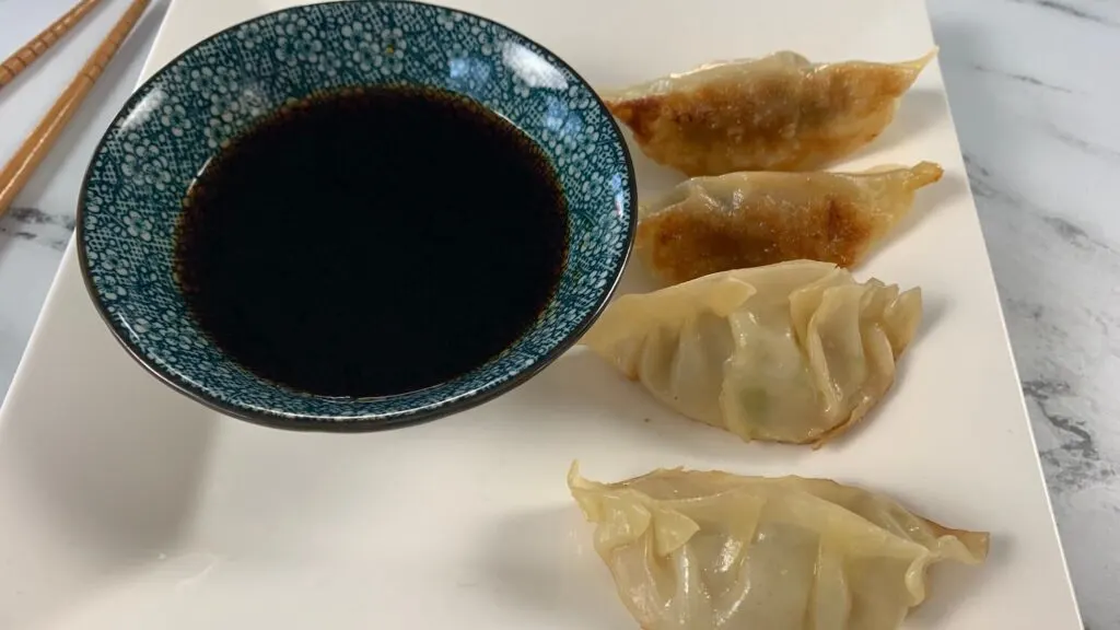 Gyozas arranged on a white plate served with gyoza sauce.