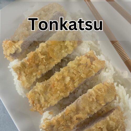 Tonkatsu vertical shot arranged on a bed of rice with chop sticks and a ramekin of katsu sauce in the background.