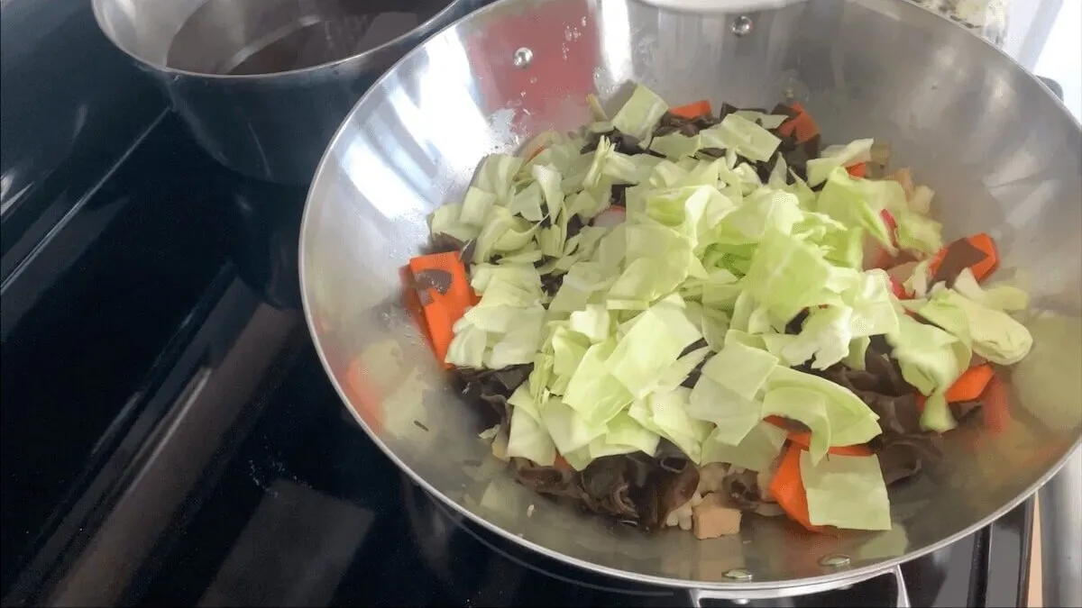 Add mushrooms, kamaboko, and cabbage to the champon mixture and cook for one minute.