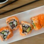 Boston roll sushi on a white sushi plate with black chopsticks
